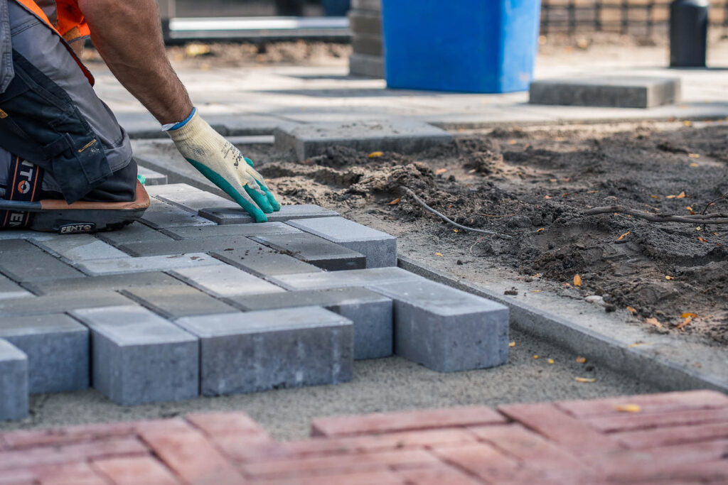 tratenmaker van Henk Verhoef legt grijze betonklinkers langs een opsluitband bij straatwerk in Voorthuizen.